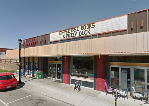 Exterior of a storefront featuring "Coffeetree Books & Fuzzy Duck" with outdoor seating and a red car parked nearby.