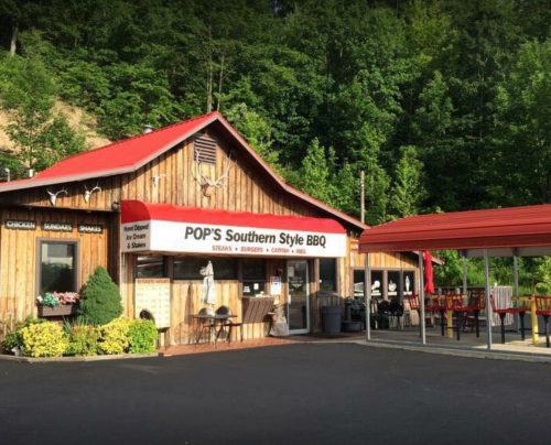 A rustic wooden building with a red awning, labeled "POP'S Southern Style BBQ," surrounded by greenery.