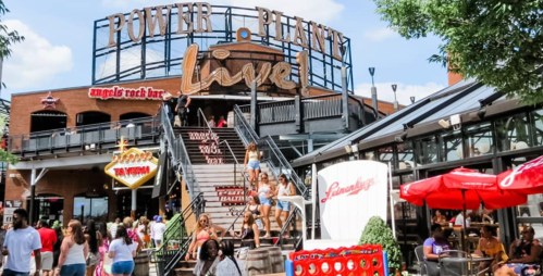 A lively outdoor scene at Power Plant Live!, featuring people walking down stairs and vibrant dining areas.