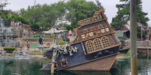 A tilted pirate ship replica near a mini-golf course, surrounded by greenery and visitors in the background.