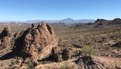 A vast desert landscape featuring rocky formations and distant mountains under a clear blue sky.