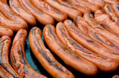 Grilled hot dogs arranged in a row, showcasing their charred, brown exterior.