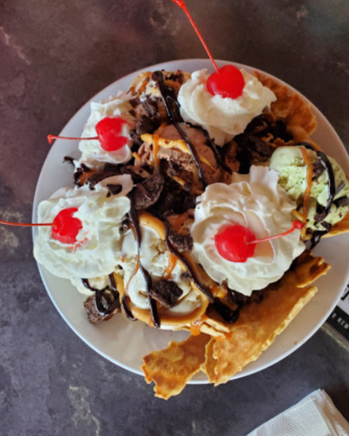 A large dessert plate with ice cream, whipped cream, chocolate sauce, crushed cookies, and cherries on top.