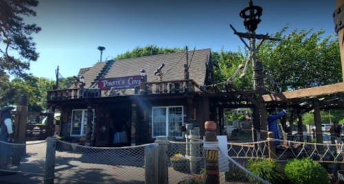 A whimsical pirate-themed shop with wooden architecture and nautical decor, surrounded by greenery and a fence.