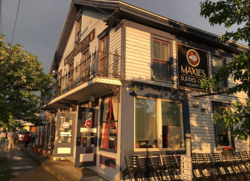 A charming restaurant exterior with a sign reading "Maxxie's Supper Club," surrounded by greenery and evening light.