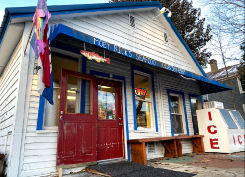A quaint seafood restaurant with a blue sign reading "Moby Rick's Seafood" and an open sign on the door.
