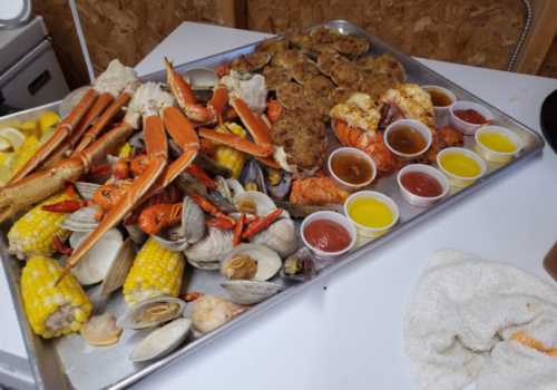 A large tray filled with seafood, including crabs, shrimp, clams, corn, and various dipping sauces.