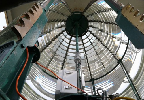 View from inside a lighthouse, showcasing the intricate glass lens and metal structure above.