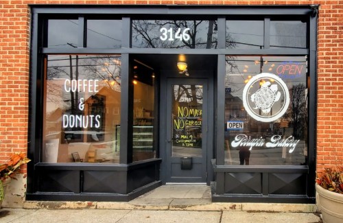 Exterior of a bakery with a sign for coffee and donuts, featuring large windows and an "OPEN" sign.