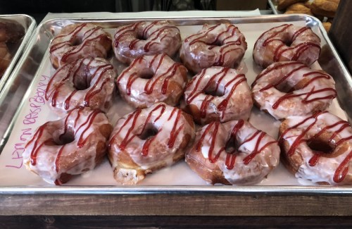 A tray of glazed donuts drizzled with red icing, arranged in two rows on a white paper.