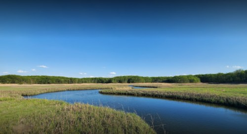 A serene landscape featuring a winding river surrounded by lush greenery and a clear blue sky.