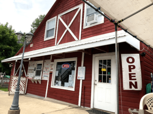 A red barn-style building with a white door and "OPEN" signs, featuring a menu display and outdoor seating area.