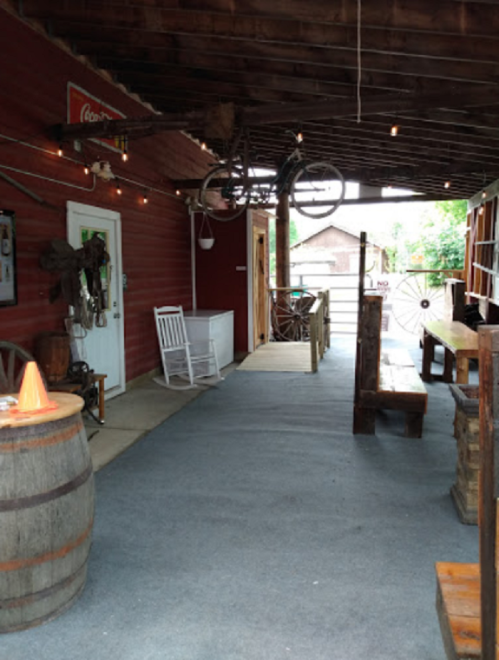 A rustic hallway with wooden benches, a barrel, and vintage decor, including a bicycle hanging from the ceiling.