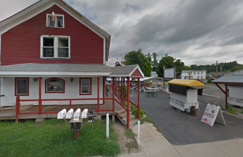 A red two-story building with a porch, surrounded by green grass and a food cart area, under a cloudy sky.