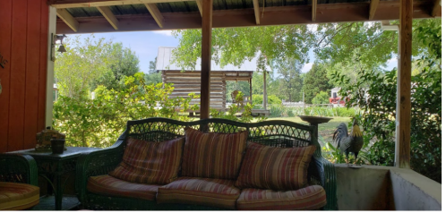 A cozy porch with a striped sofa, overlooking a lush garden and a pond in the background.