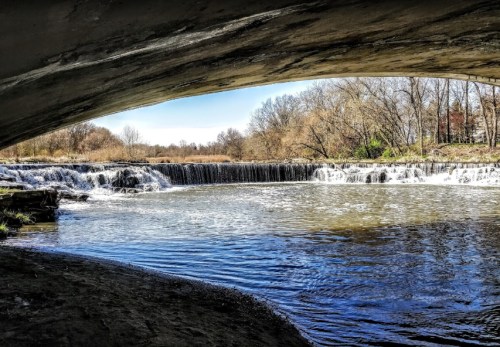 A serene view of a waterfall framed by an arch, with trees and clear blue sky in the background.