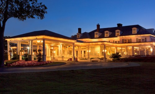 A beautifully lit mansion at dusk, featuring a grand entrance and lush landscaping.