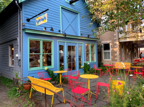Colorful outdoor seating area in front of a blue building with a sign that reads "Fortunes." Brightly colored chairs and tables.