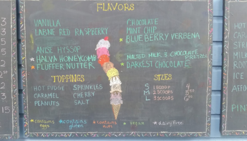 Chalkboard menu displaying ice cream flavors, toppings, and sizes with prices.