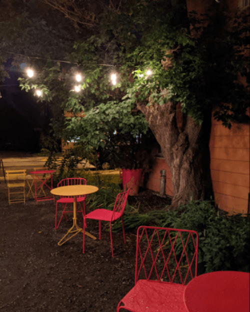 A cozy outdoor seating area at night, featuring colorful chairs and string lights hanging above a tree.