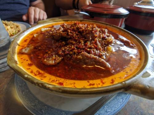 A spicy dish with tender meat and a rich, red chili sauce served in a clay pot, garnished with chili flakes.