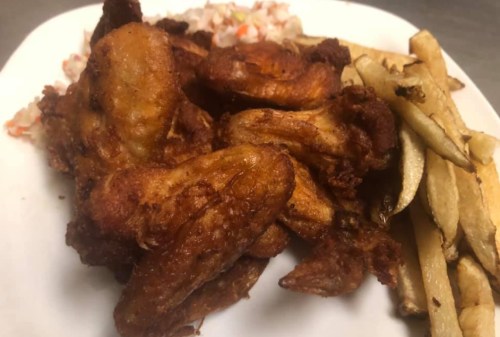A plate of crispy fried chicken wings served with French fries and a side of coleslaw.