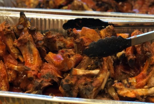 A close-up of grilled ribs coated in sauce, with tongs picking up a piece from a tray.