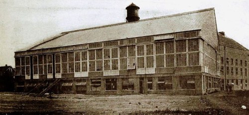 Historic black-and-white photo of a large, industrial building with many windows and a water tower on the roof.