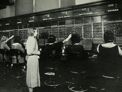 A vintage telephone exchange with women operating switchboards, connecting calls in a bustling office setting.