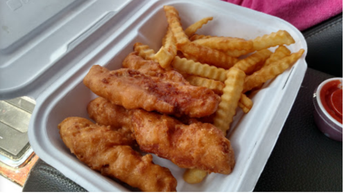 A takeout container with crispy fried chicken strips and crinkle-cut fries, accompanied by a small cup of dipping sauce.