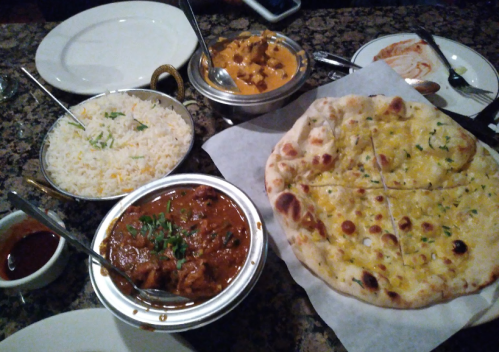 A table spread with Indian dishes: butter chicken, rice, naan, and a curry, with sauces on the side.