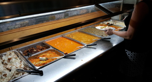 A person serving food from a buffet with various dishes, including rice, lentils, and sauces, alongside bread.