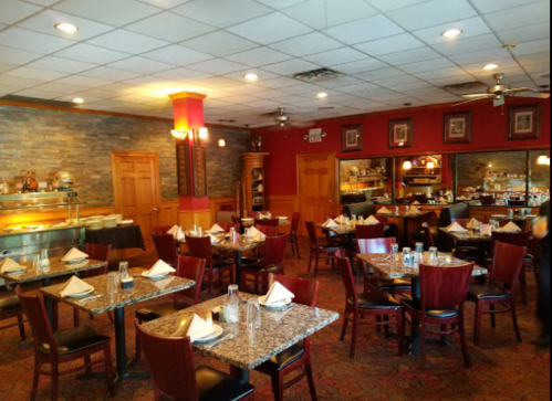 Interior of a restaurant featuring tables set with napkins, a buffet area, and warm lighting.