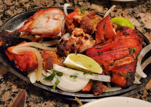 Sizzling platter of grilled chicken with onions, lime, and colorful vegetables on a stone surface.