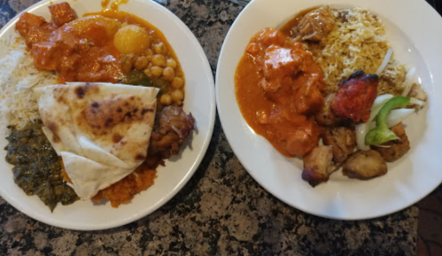 Two plates of Indian food: one with rice, curry, naan, and chickpeas; the other with chicken, rice, and grilled vegetables.