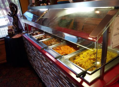 A buffet display with various dishes, including rice and curries, under a glass cover in a restaurant setting.