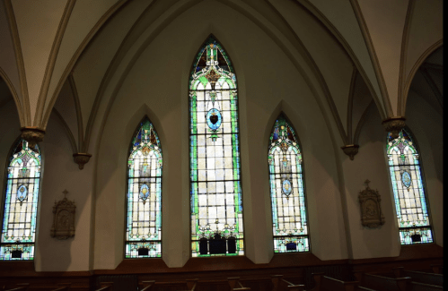 Interior of a church featuring tall stained glass windows with intricate designs and colorful patterns.