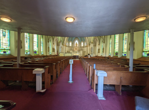 Interior of a church featuring wooden pews, stained glass windows, and a red carpet leading to the altar.