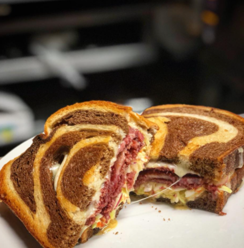 A sliced sandwich featuring layers of pastrami and cheese between swirled rye and pumpernickel bread.