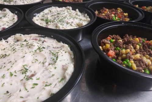 Bowls of creamy mashed potatoes topped with herbs and bowls of seasoned ground beef with mixed vegetables.
