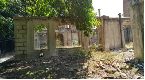 Ruins of a stone structure overgrown with vegetation, featuring arched openings and scattered debris.