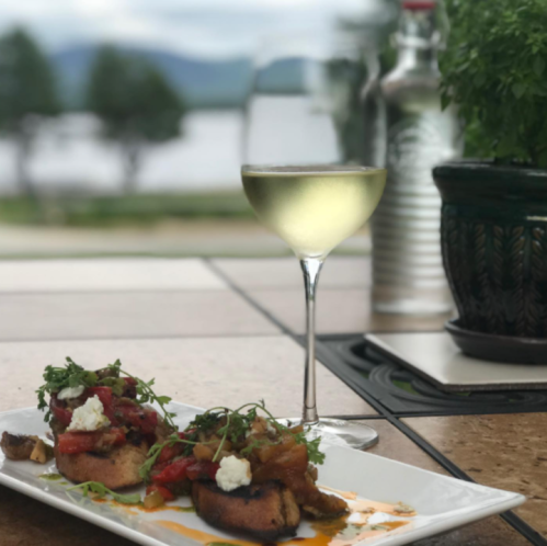 A plate of bruschetta topped with tomatoes and herbs, alongside a glass of white wine, with a scenic background.