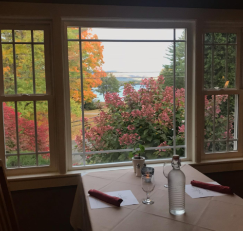 A cozy dining table by a window, showcasing vibrant fall foliage and a serene view of the water outside.