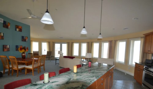 Spacious modern kitchen and dining area with large windows, wooden furniture, and a marble countertop.