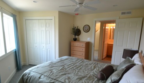 Cozy bedroom with a large bed, dresser, and doors leading to a closet and bathroom. Natural light from windows.