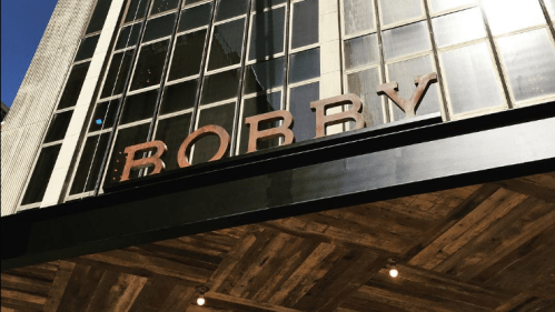Sign reading "BOBBY" on a modern building with large windows and a wooden overhang.