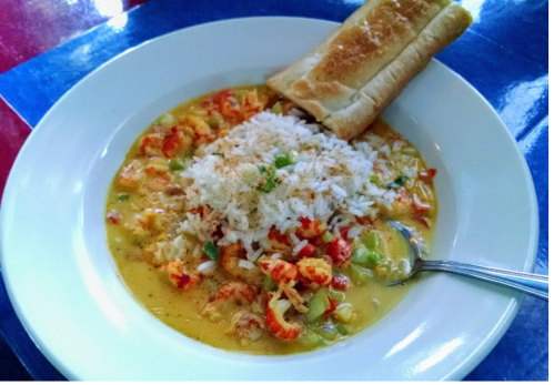 A bowl of seafood gumbo with rice and vegetables, served with a piece of toasted bread on the side.