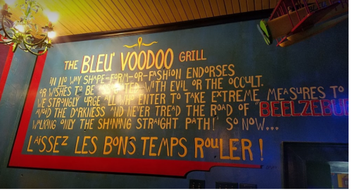 Colorful wall mural at Bleu Voodoo Grill, featuring a playful warning about evil and a call to enjoy life.