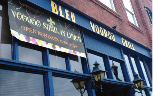 Sign for Voodoo Grill advertising Sunday lunch hours, with colorful decorations, on a brick building.