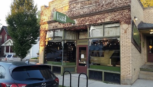 A cozy restaurant named "Toast" with large windows, greenery, and a vintage brick exterior. A car is parked nearby.